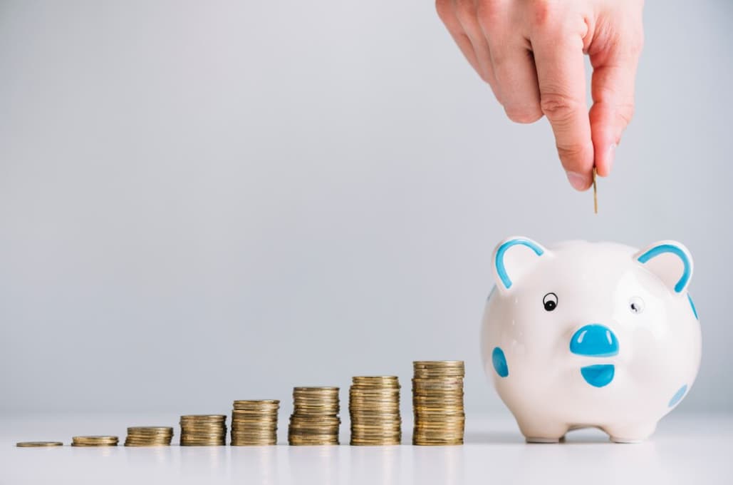 Hand inserting a coin into a piggy bank with a growing coin stack