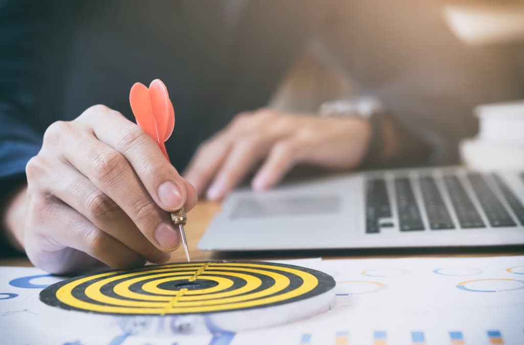 A person holding a dart aiming at the center of a target over charts