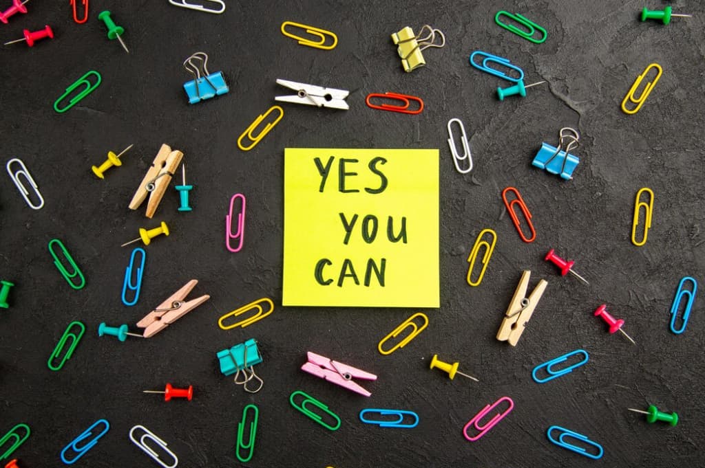 A sticky note with 'YES YOU CAN' surrounded by colorful paperclips