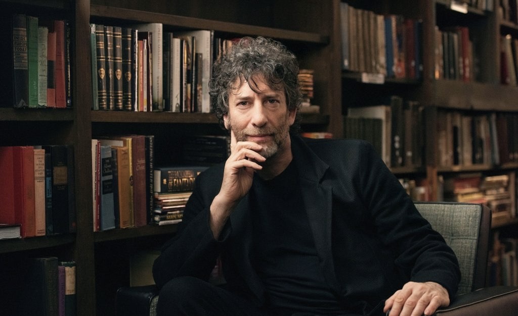 Neil Gaiman sits in front of books